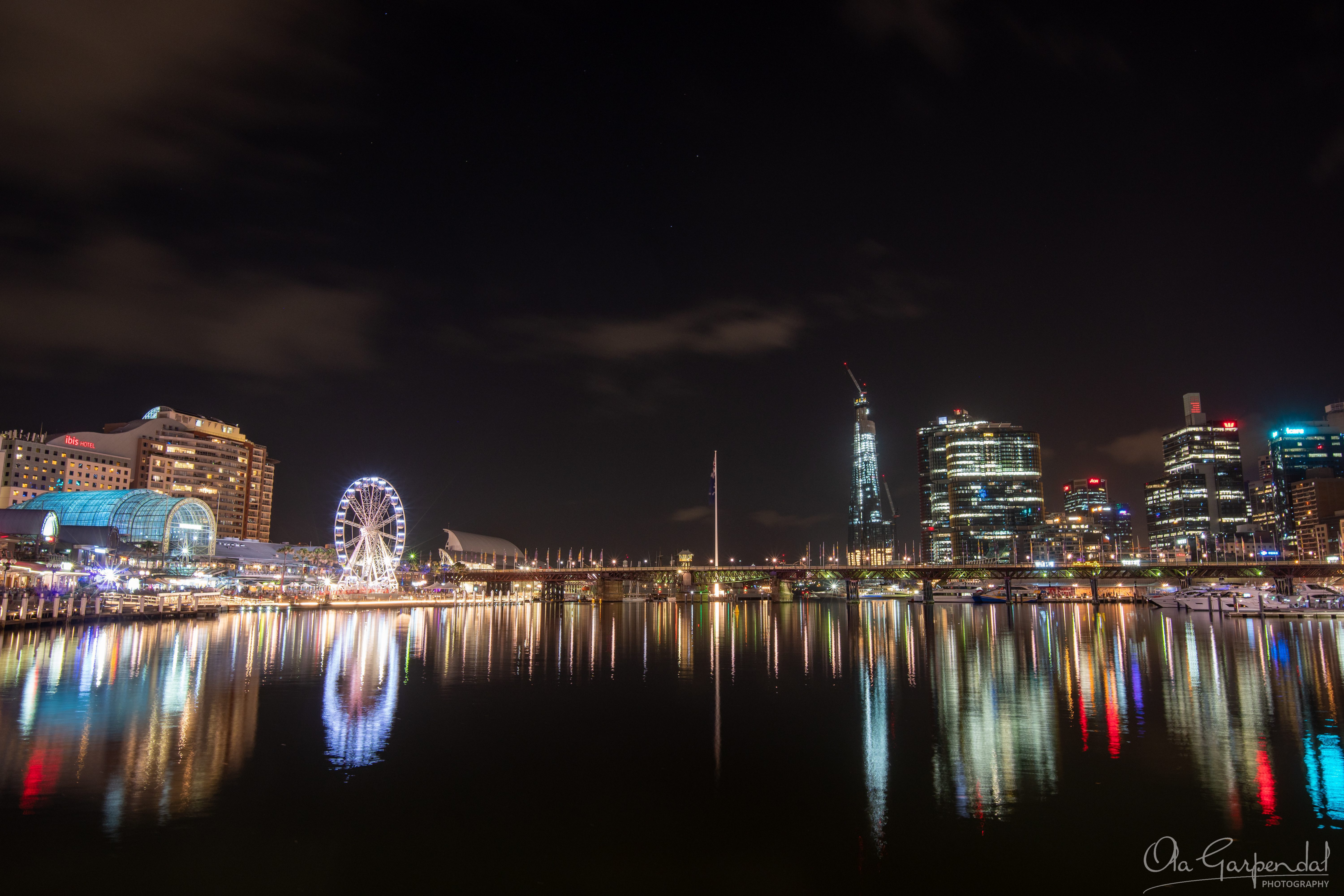 Darling Harbour Night Lights showing Sydney's illuminated waterfront, Ferris wheel, city skyline, marina and colourful reflections on calm harbour waters during a February evening, photographed by Ola Garpendal Photography