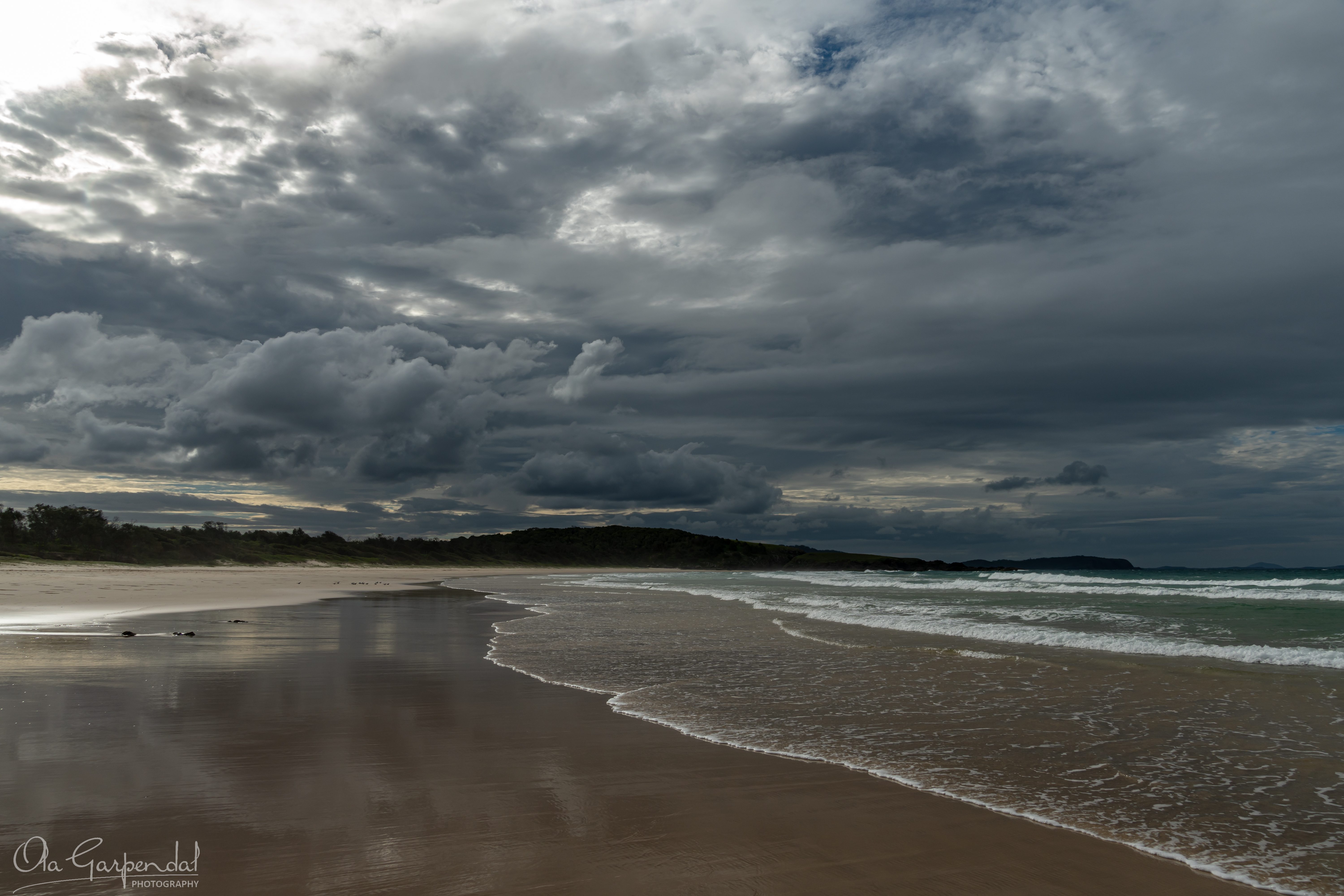 Moody Afternoon featuring Delicate Nobby on the Mid North Coast, with a sweeping beach, reflective wet sand, rolling surf, dramatic storm clouds and subdued coastal tones in May, photographed by Ola Garpendal Photography