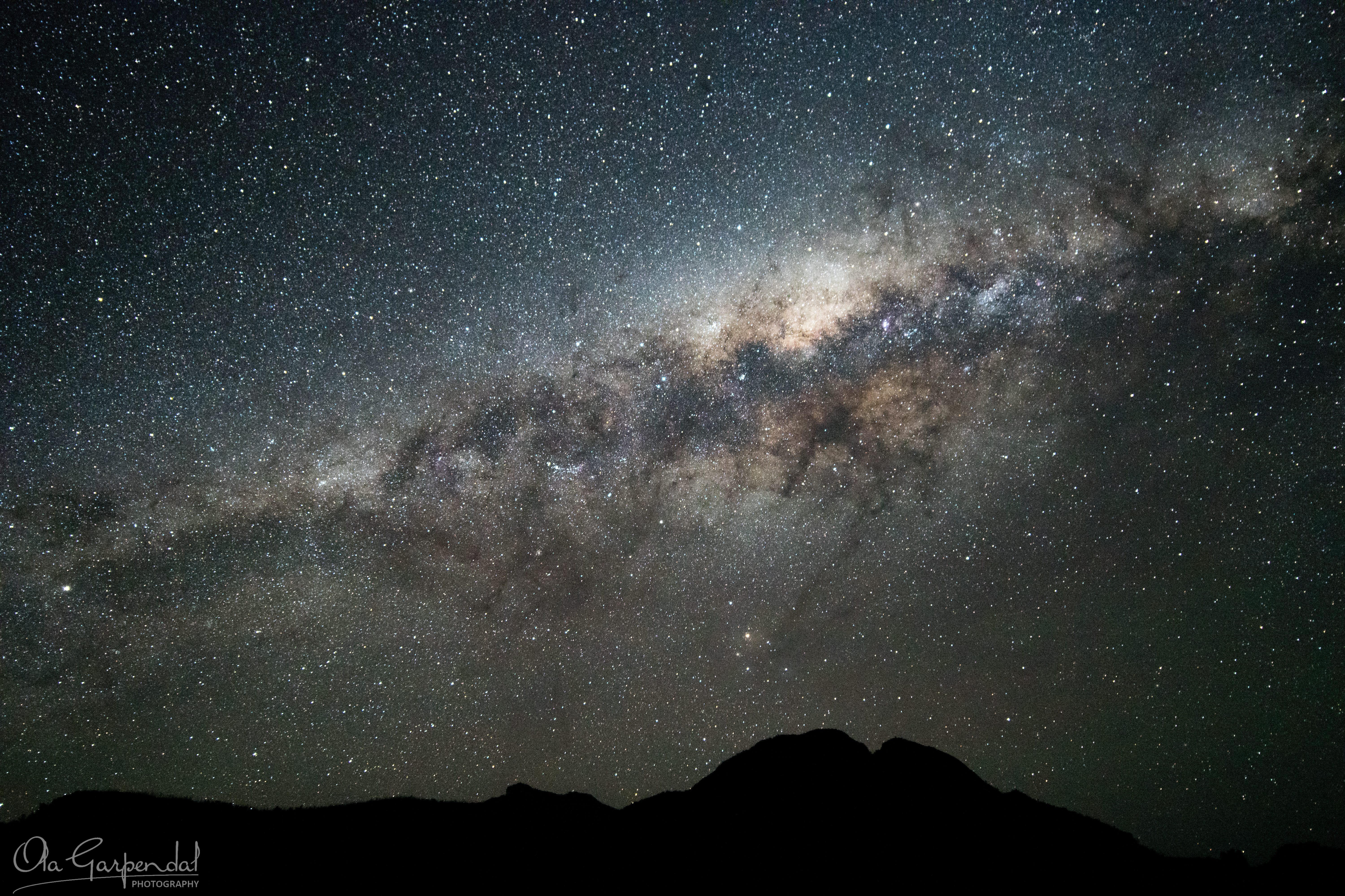 Warrumbungle Night Sky showing the Milky Way arching above the silhouetted peaks of the Warrumbungle Range, with dense star fields, dark dust lanes and a crystal-clear July night sky at 3 am, photographed by Ola Garpendal Photography