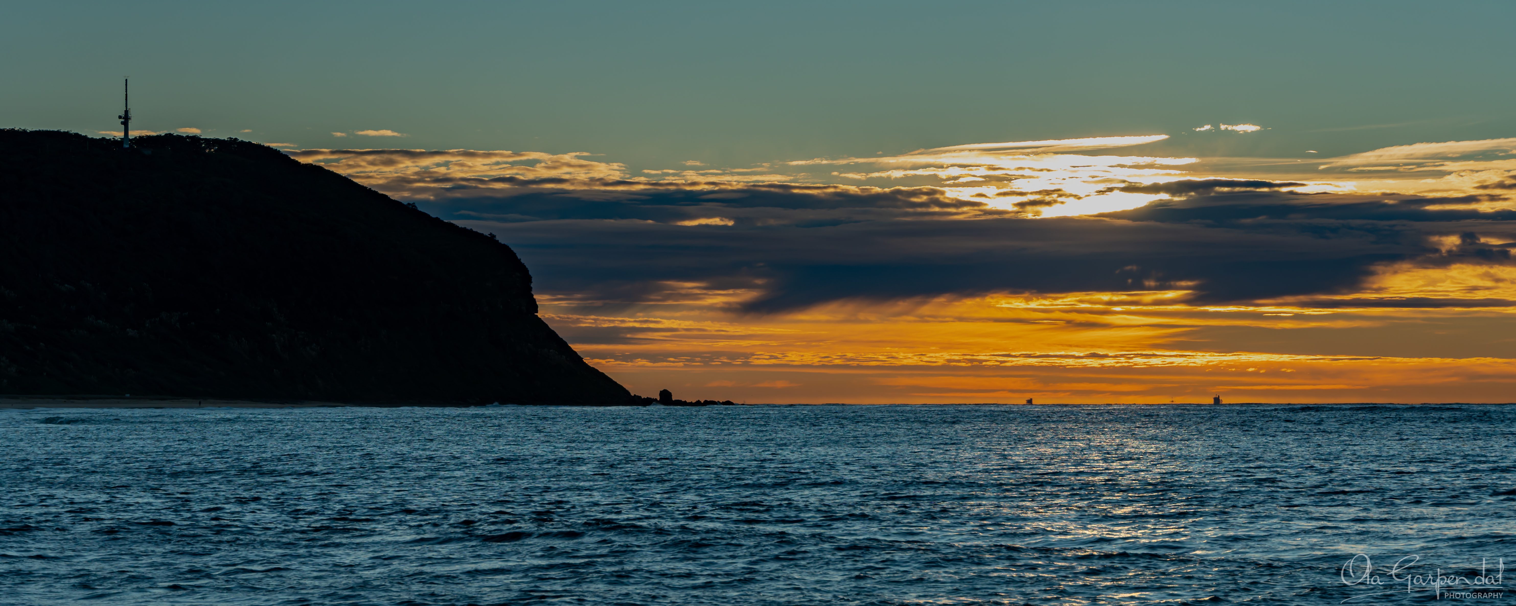 Sunrise at Forresters Beach, after the sunrise, the sky is amber and gold, the headland is in silhouette, photographed by Ola Garpendal Photography
