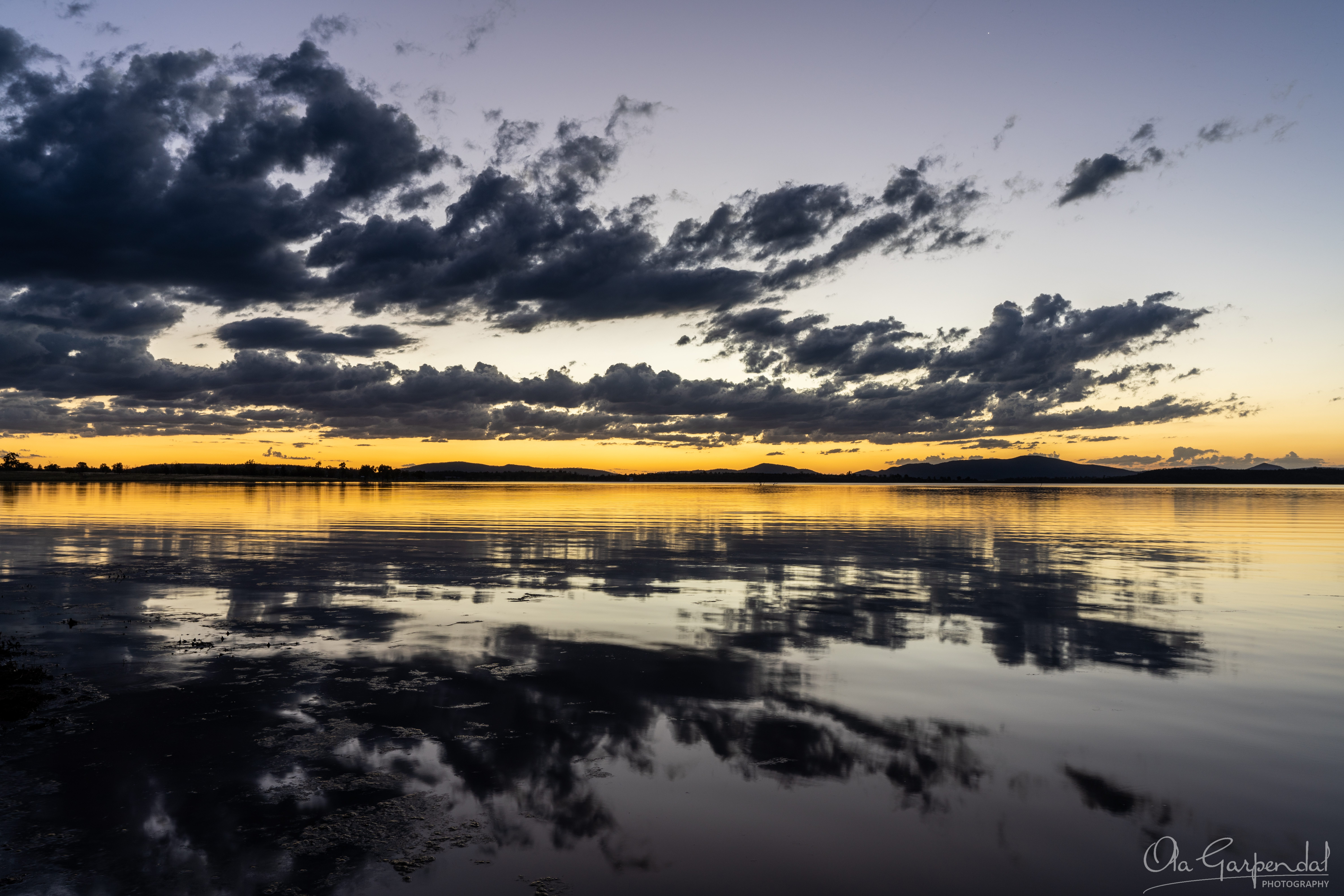 Evening Glow, narrow yellow band along the horizon, reflected in the still water, photographed by Ola Garpendal Photography