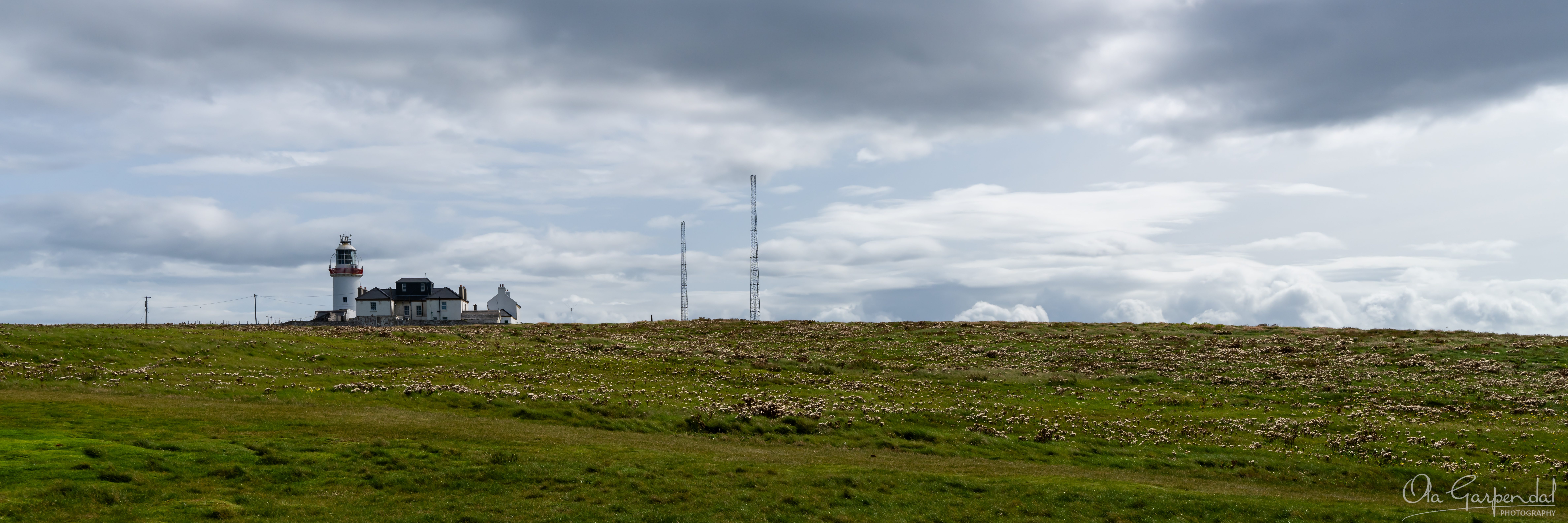 Loophead Lighthouse, a lighthouse in the distance with rocky foreground, photographed by Ola Garpendal Photography