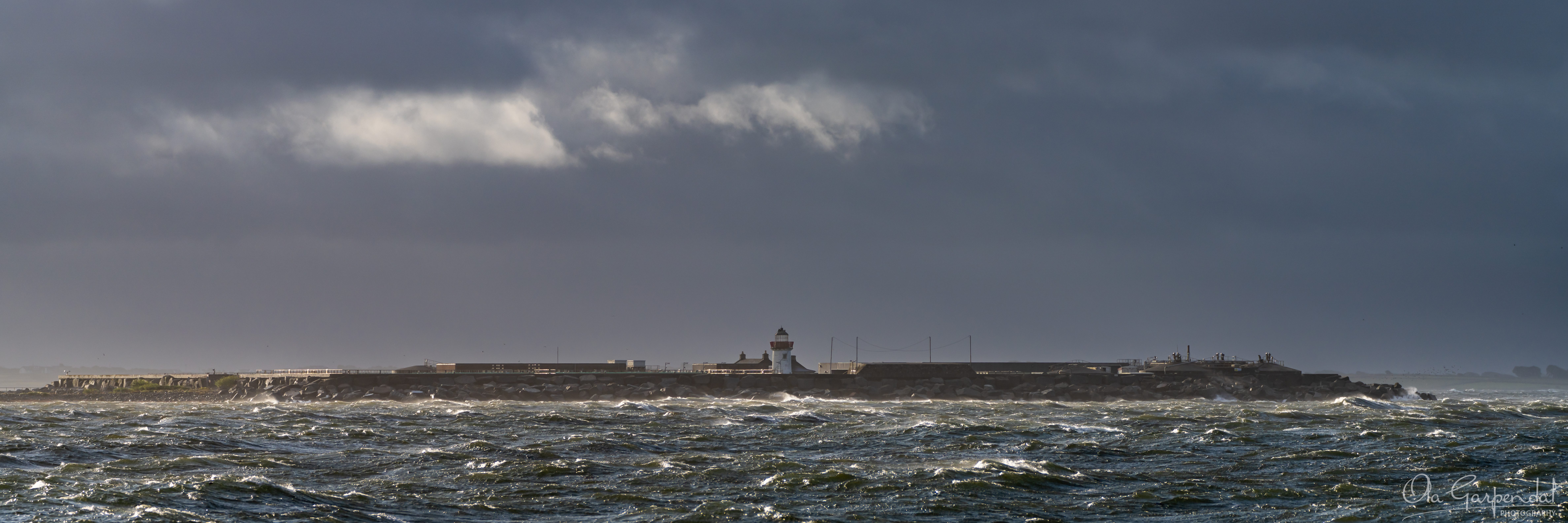 Mutton Island Lighthouse, red-and-white lighthouse under a dramatic storm sky and rough Atlantic swells, photographed by Ola Garpendal Photography