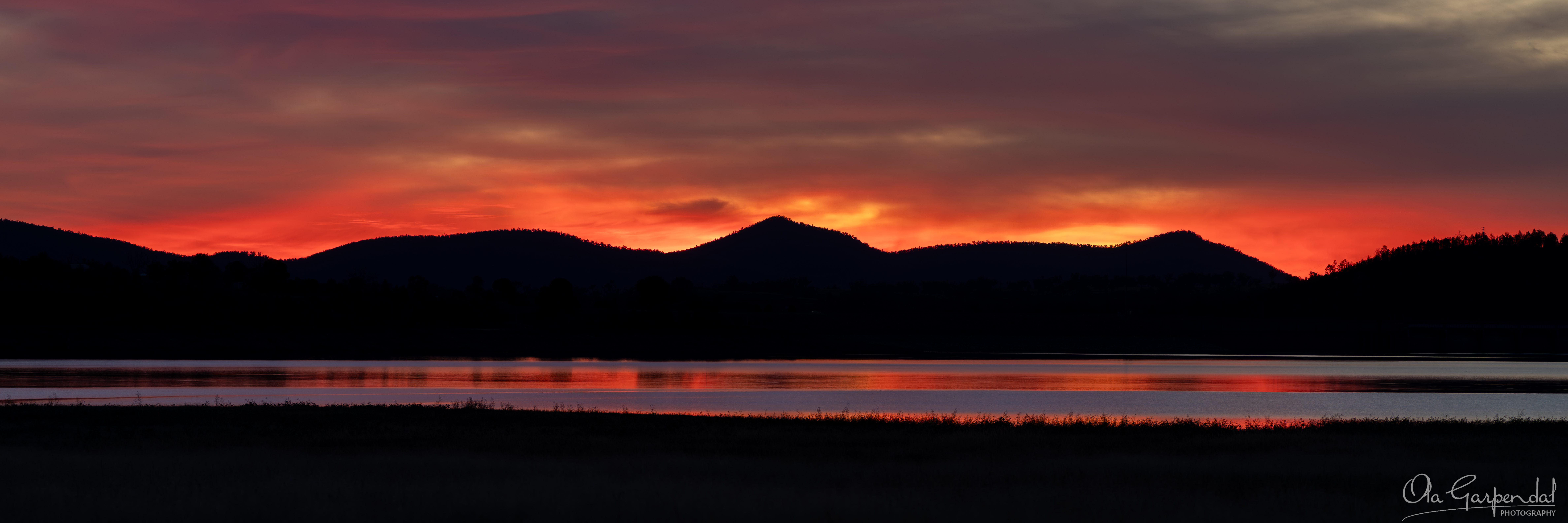 Fiery Sky showing a brilliant crimson and red post-sunset glow above silhouetted hills at Lake Keepit, with reflections across still water and layered twilight colours in April, photographed by Ola Garpendal Photography