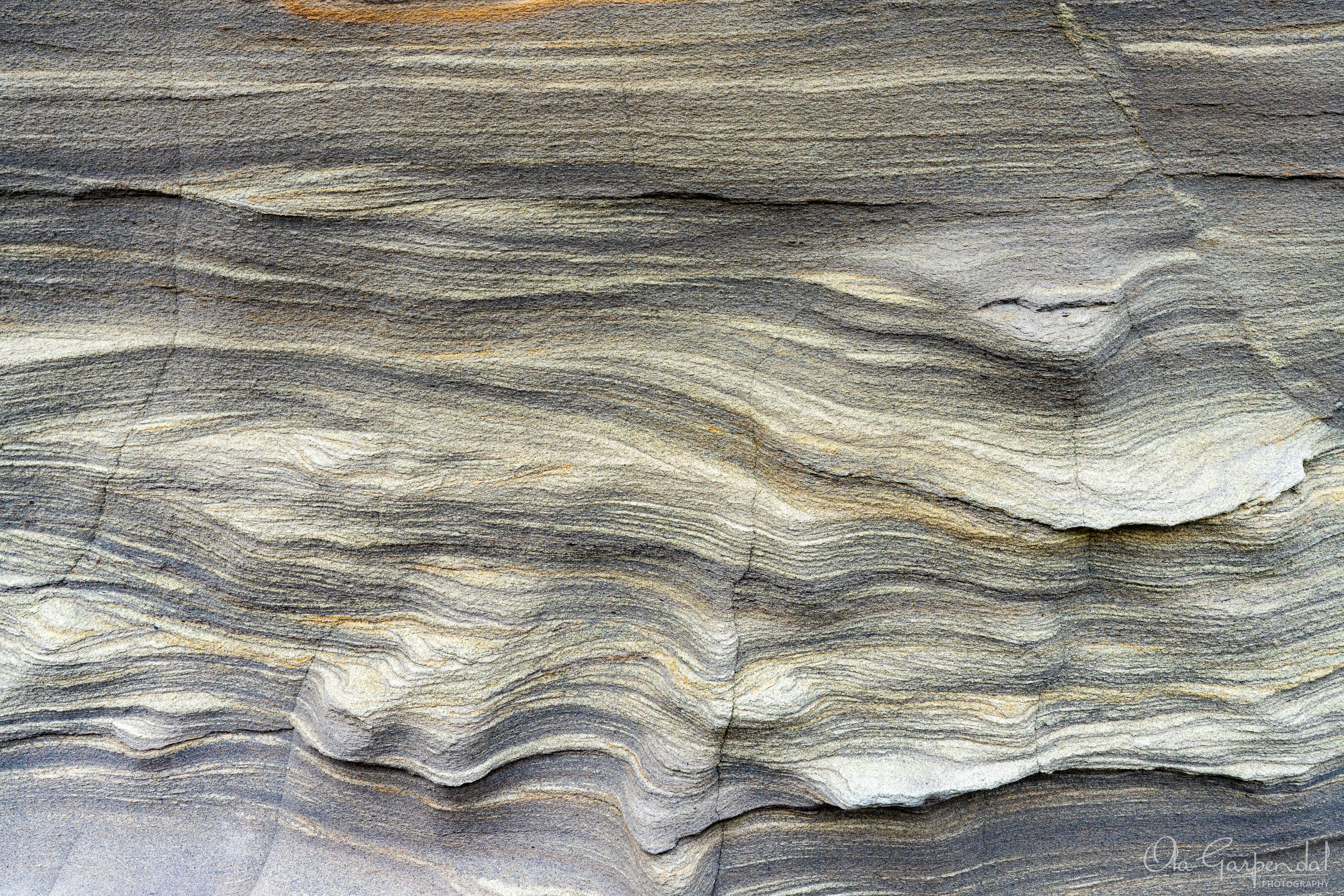 “Rock Streaks” — a close‑up abstract view of layered coastal rock with horizontal streaks and fine textures, photographed by Ola Garpendal Photography